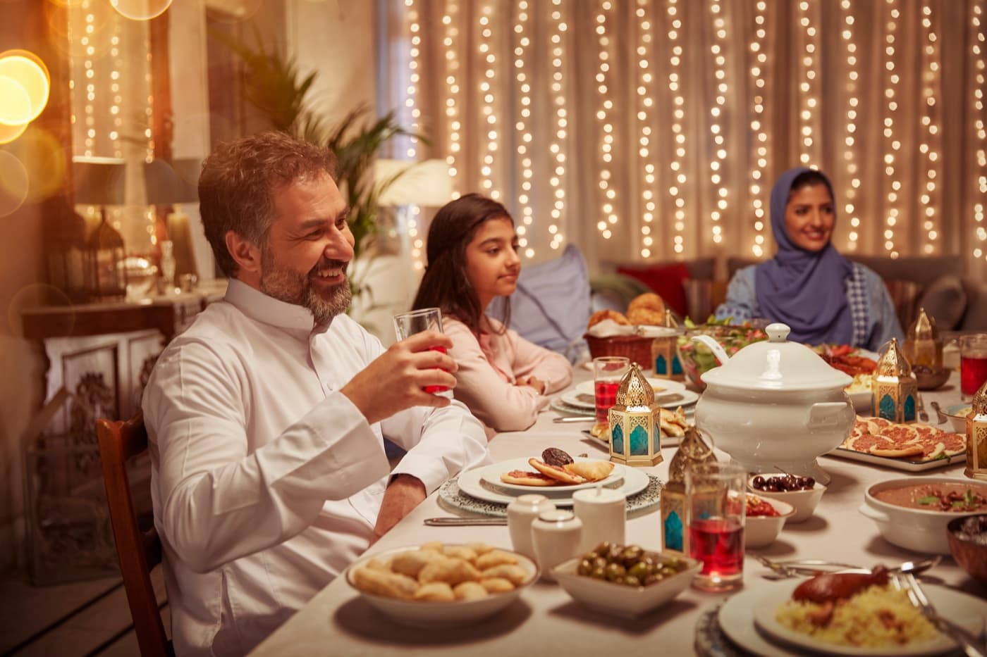 A family around a table hung with string lights, glasses of orange drink poured.