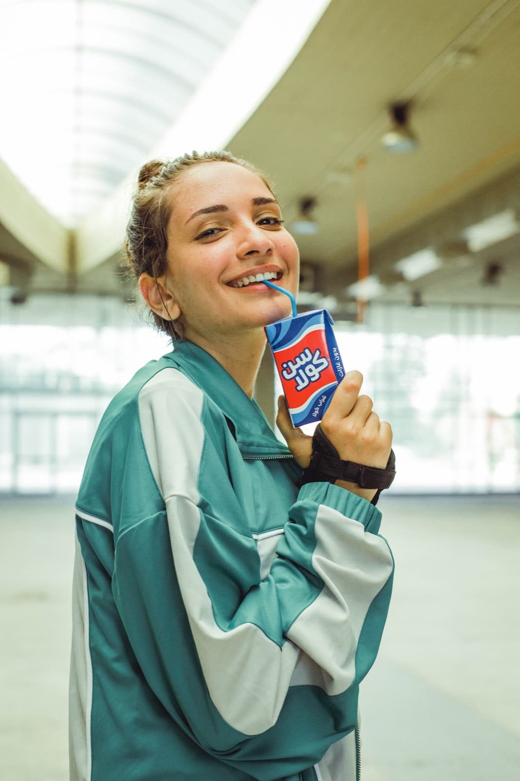 A young woman in a teal tracksuit drinking from a Suncola carton through a straw.