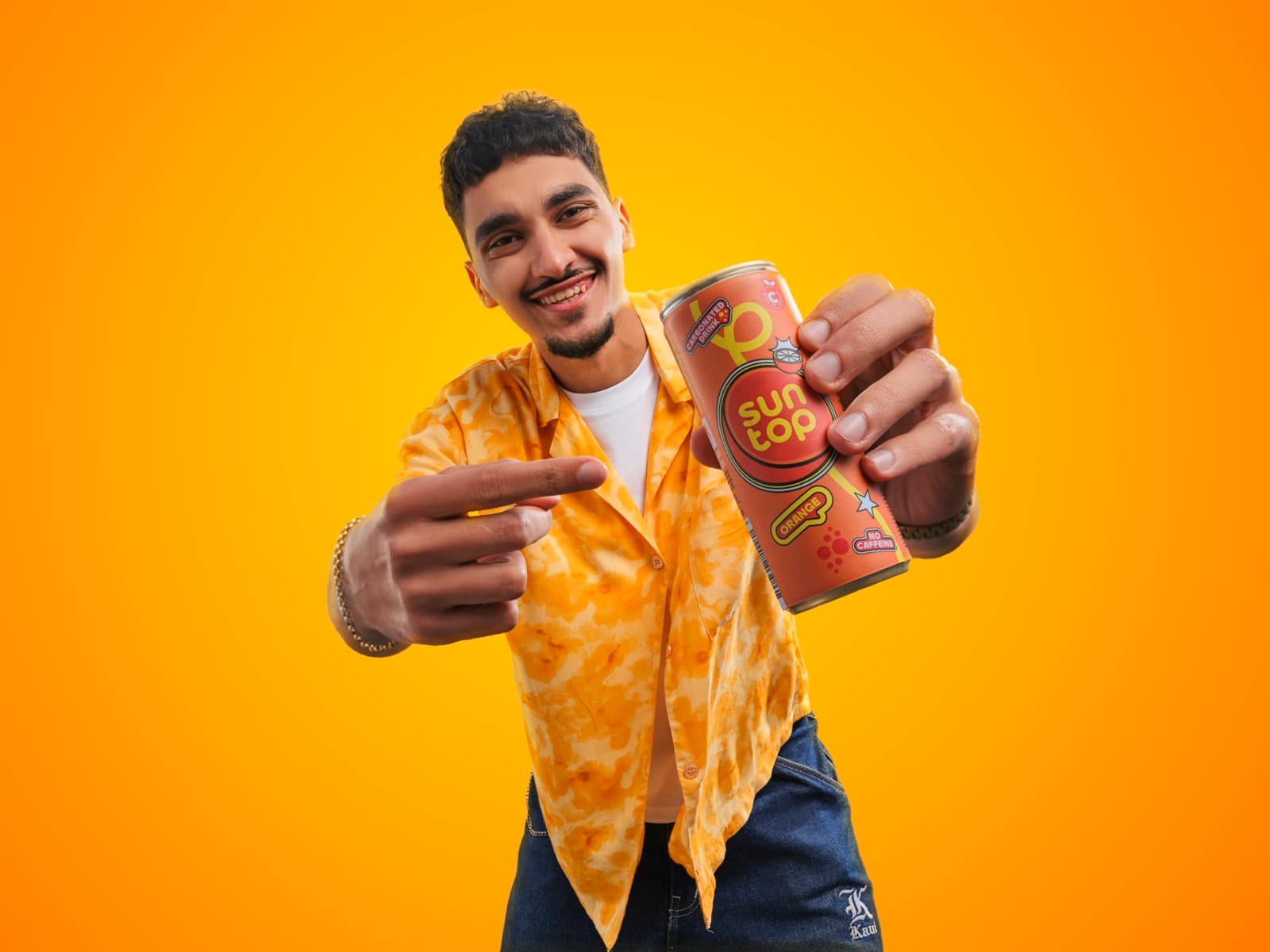 A young man in a tie-dye shirt holding a Suntop can out to the camera against a yellow ground.