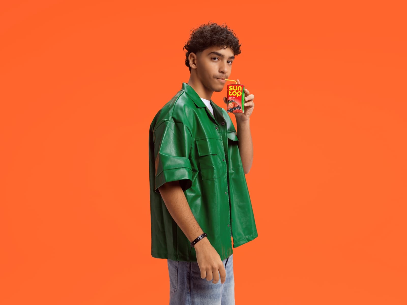 A young man in a green shirt against an orange ground, holding a Suntop carton.